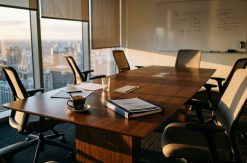 Meeting room after everyone has left: a printed proposal still squared on the table, a cold half-finished coffee beside...