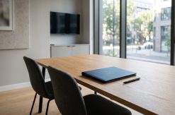 Quiet commercial meeting room with two chairs drawn up to a table, a closed folder and a pen on the surface, natural...